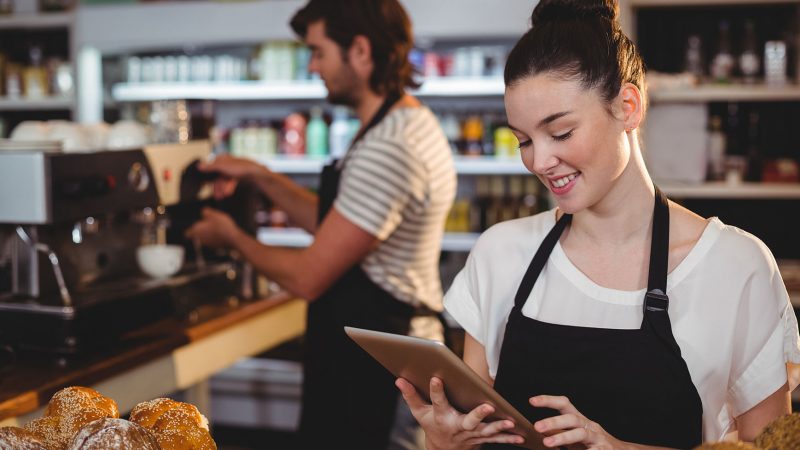 Smiling waitress standing at counter using digital tablet