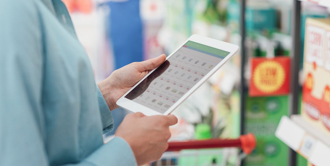 Woman shopping at the supermarket, she is connecting with her digital tablet and searching offers online, hands close up